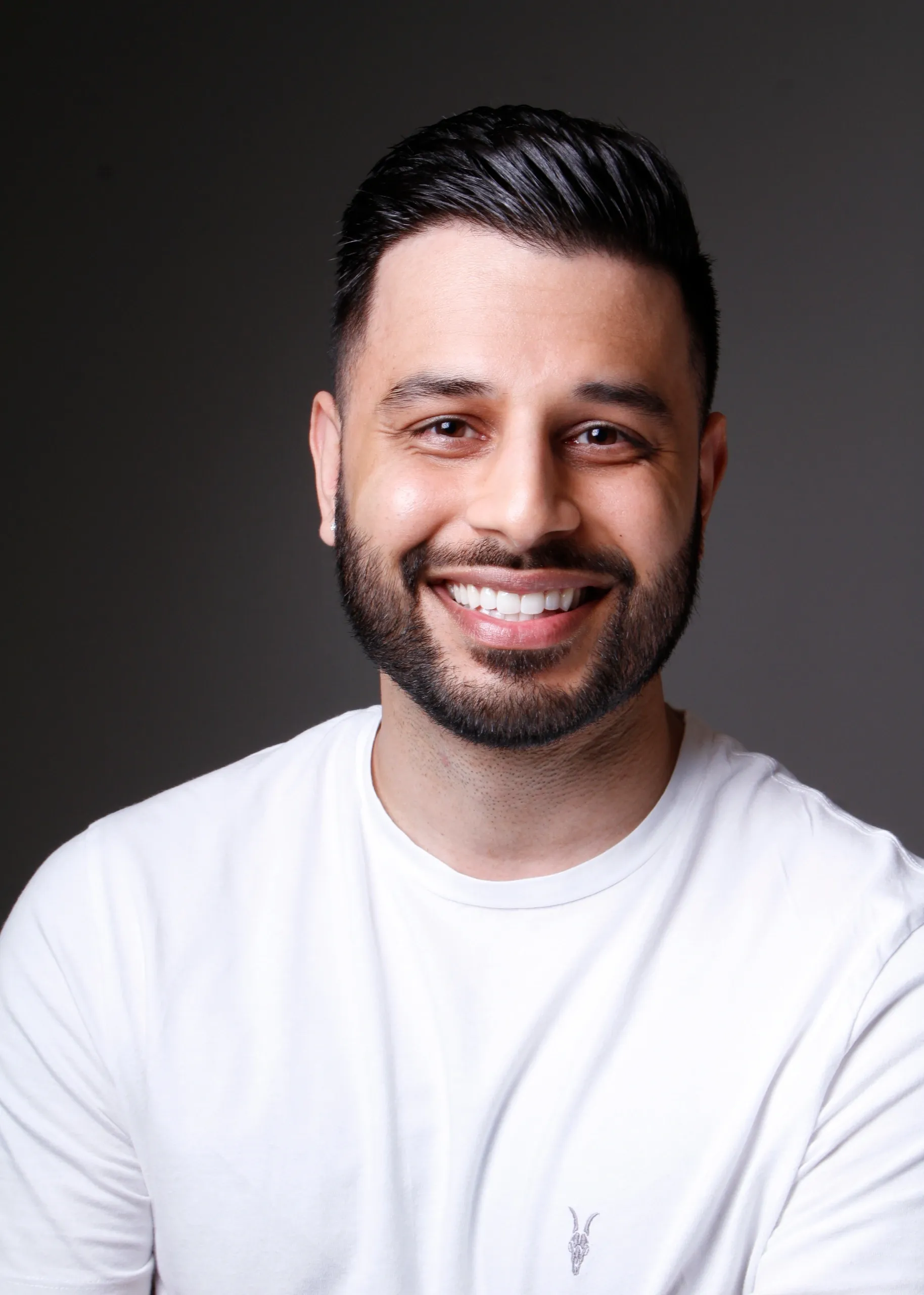 Man with dark hair and beard smiling, wearing a white t-shirt, posed against a plain dark background—perfect for a civil law attorney profile.